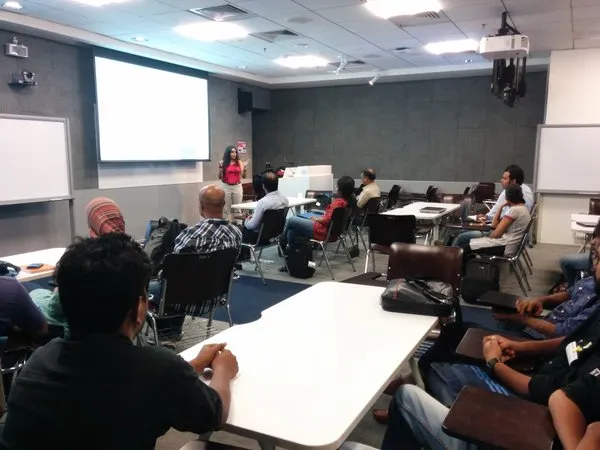 A meeting room at the Google office in Bangalore: a speaker stands at the front beside a projector screen while workshop attendees sit at tables facing her.